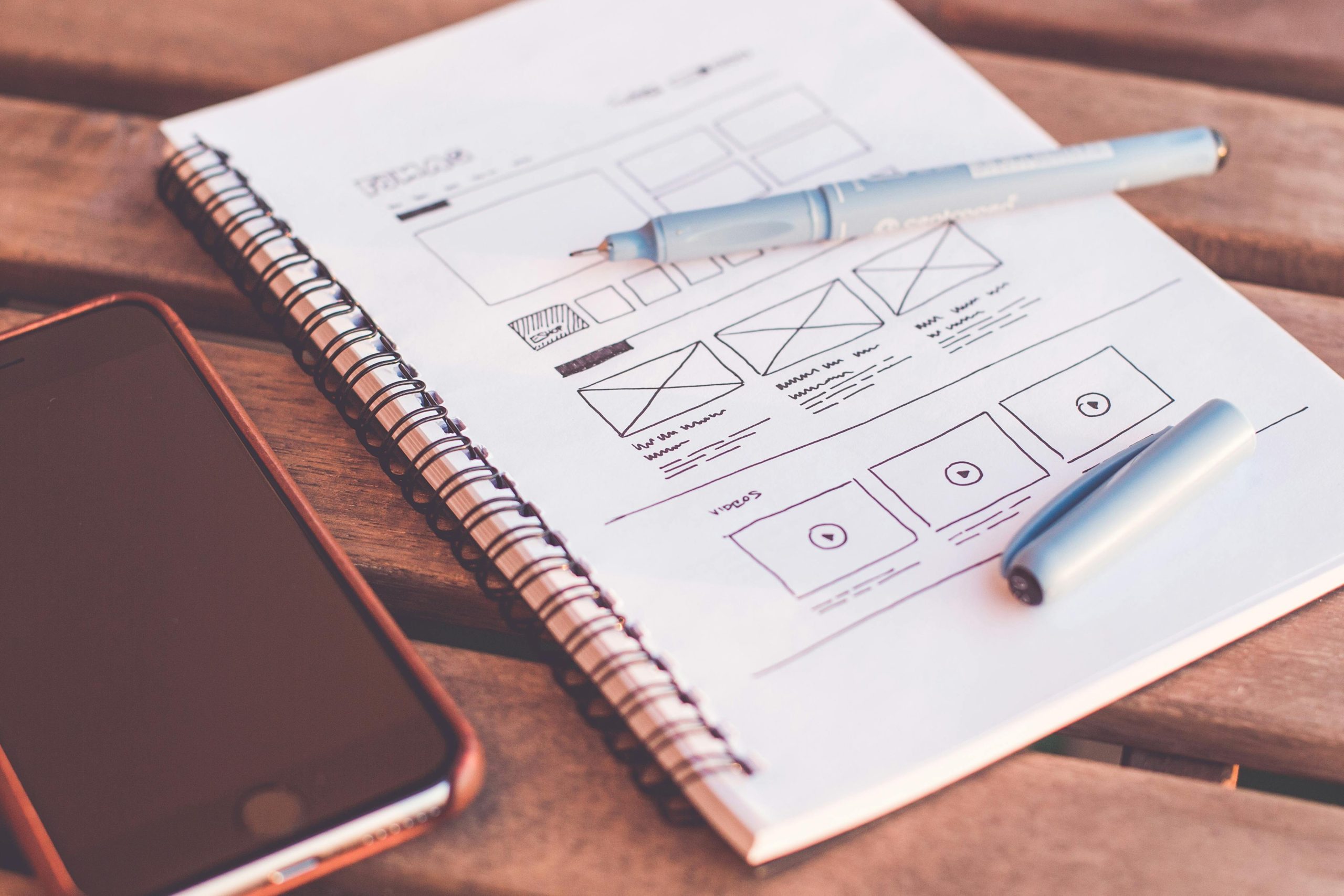 digital Close-up of a notebook with wireframe sketches and a smartphone on a wooden desk.